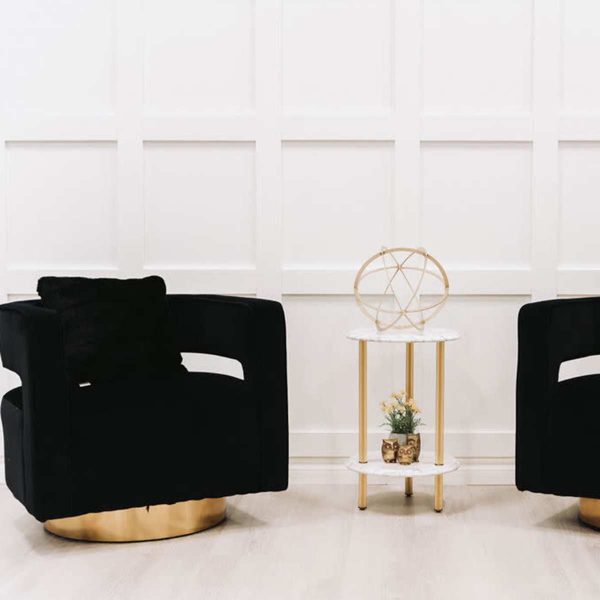 A pair of black upholstered swivel chairs facing each other, with a small marble-top side table between them featuring decorative items.
