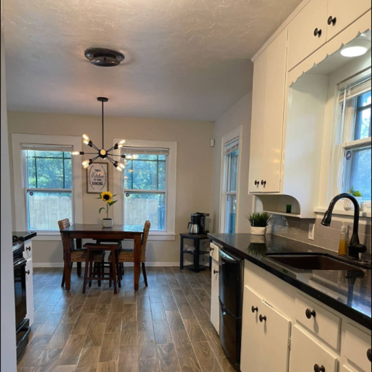 A bright kitchen features black countertops, white cabinets, and a dining table set for four near a window.