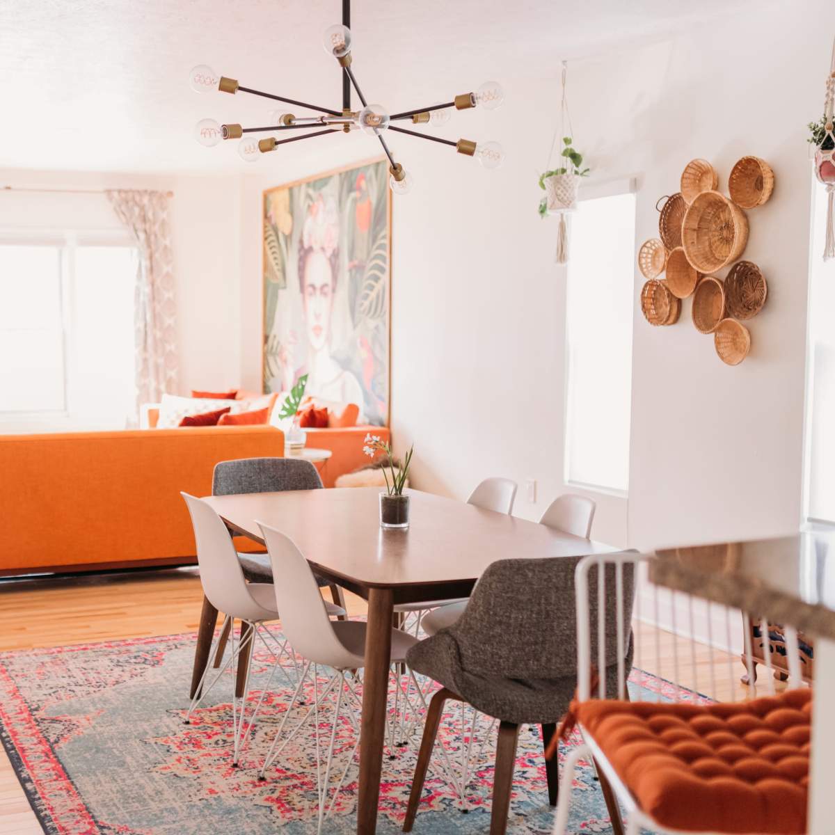 A bright living and dining area featuring orange furniture, a dining table with modern chairs, and decorative wall art.