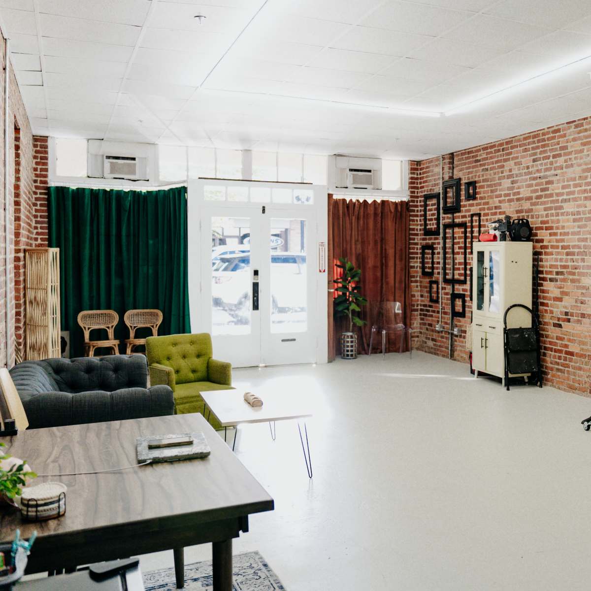 A spacious room with brick walls, featuring a green couch, a wooden table, and a folding partition on wheels.