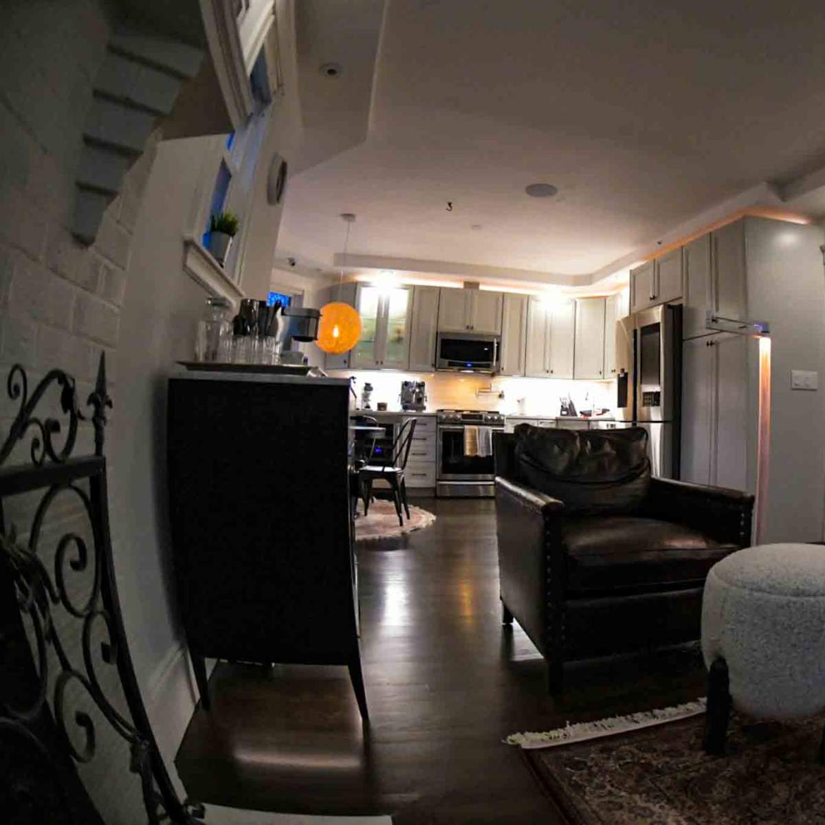 A modern living space with an open kitchen area and a seating area featuring a dark leather chair and a light-colored ottoman.