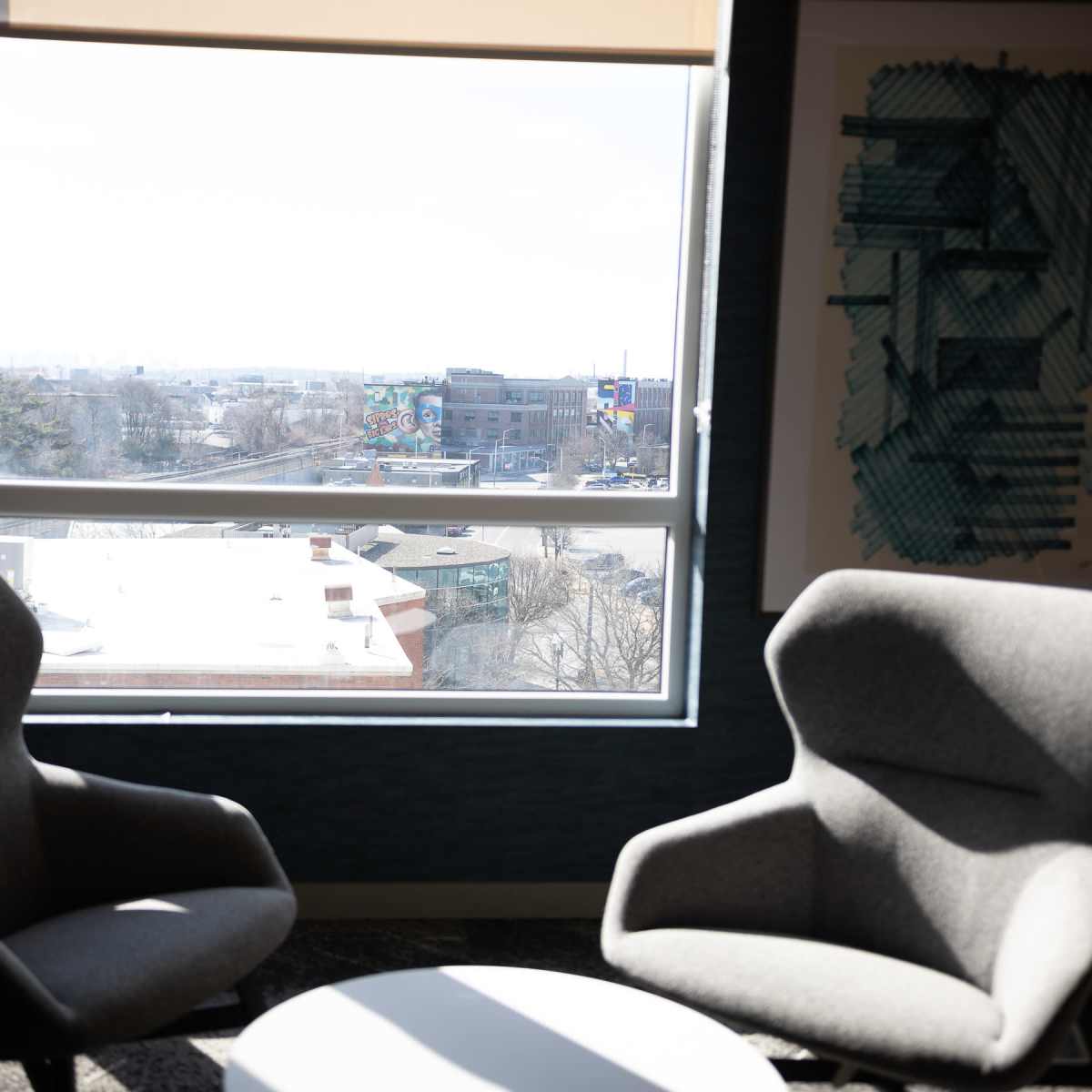 Two gray armchairs positioned near a large window, overlooking an outdoor view of a cityscape with buildings and greenery.