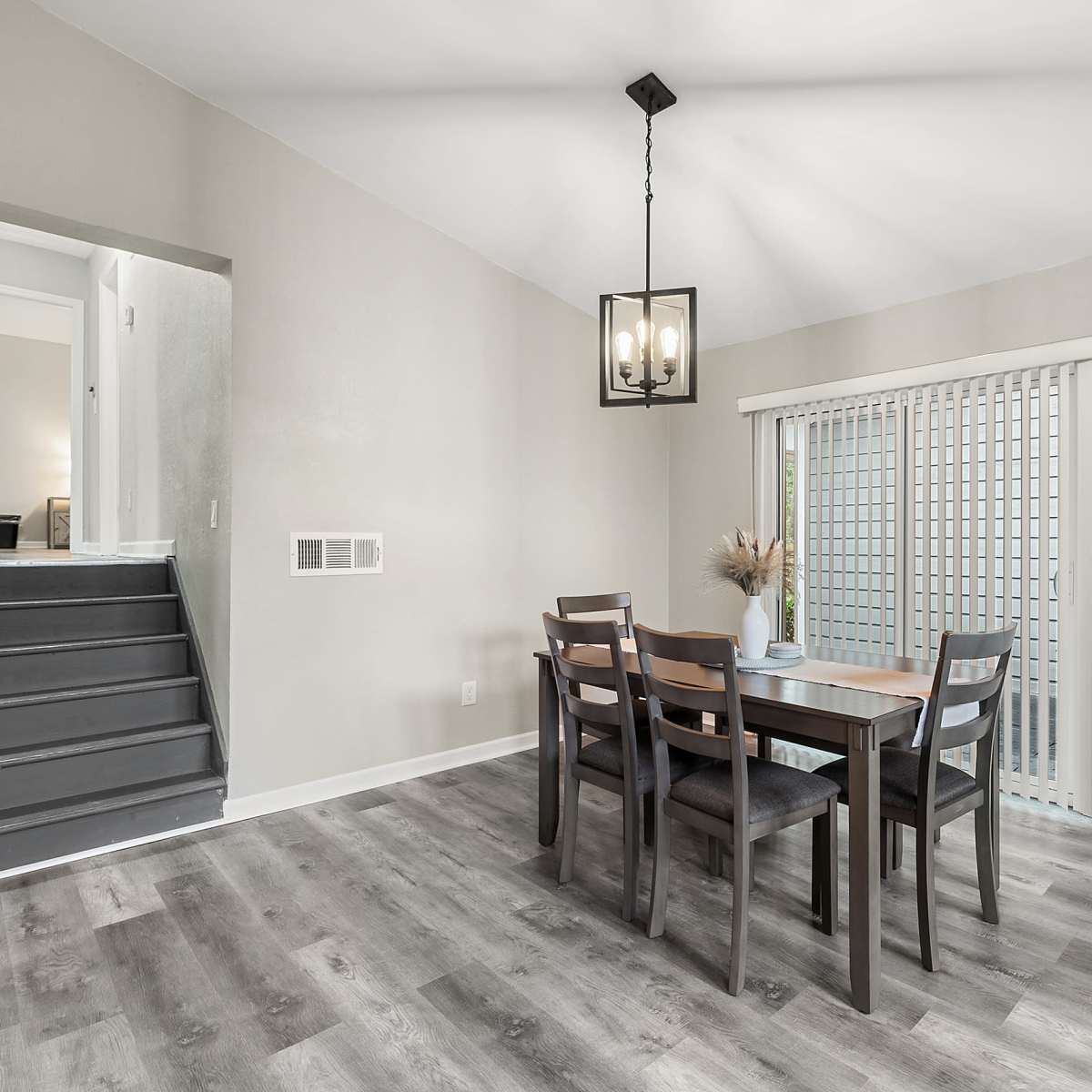 A dining area features a wooden table with six chairs, a pendant light overhead, and a door leading to an outdoor space.