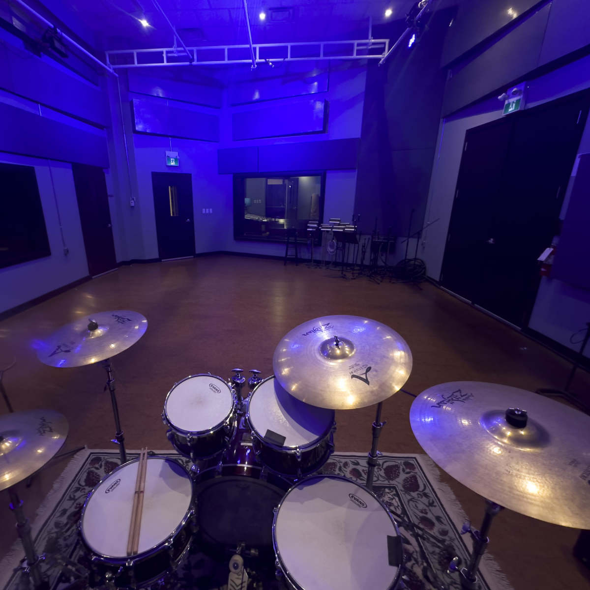 A view of a music studio from behind a drum set, featuring purple lighting and soundproof walls.