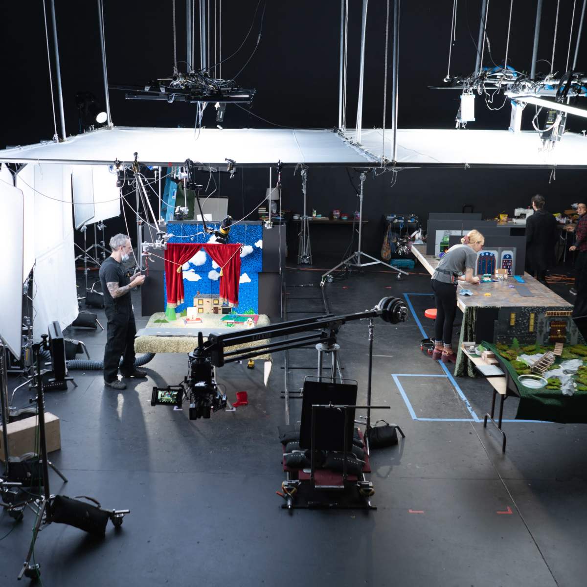 A film set is arranged with lighting equipment and props, featuring two crew members working on different diorama scenes.