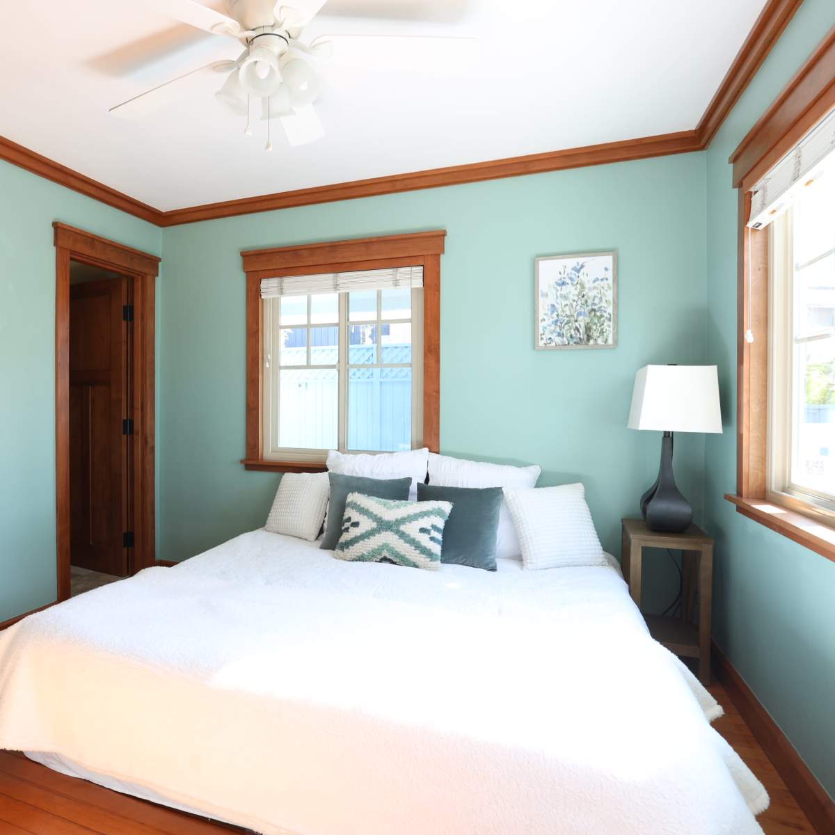 A simple bedroom featuring a bed with white bedding, a decorative pillow, a nightstand with a lamp, and wooden closet doors.