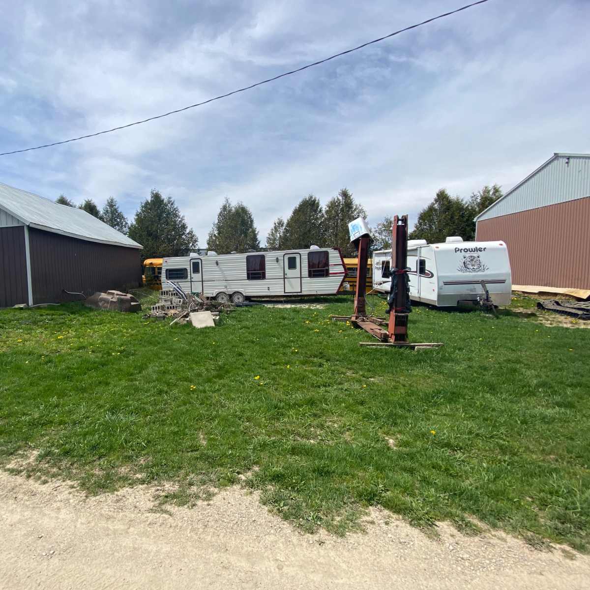 A grassy area with a trailer, a small truck, and a piece of equipment near two barns.