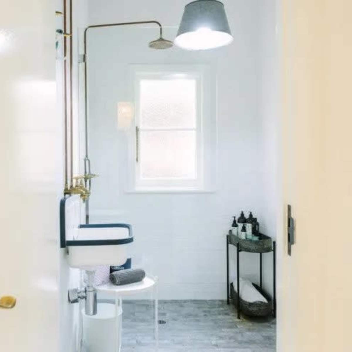 A clean, minimalist bathroom with a shower, a modern toilet, and a small storage cart containing toiletries.