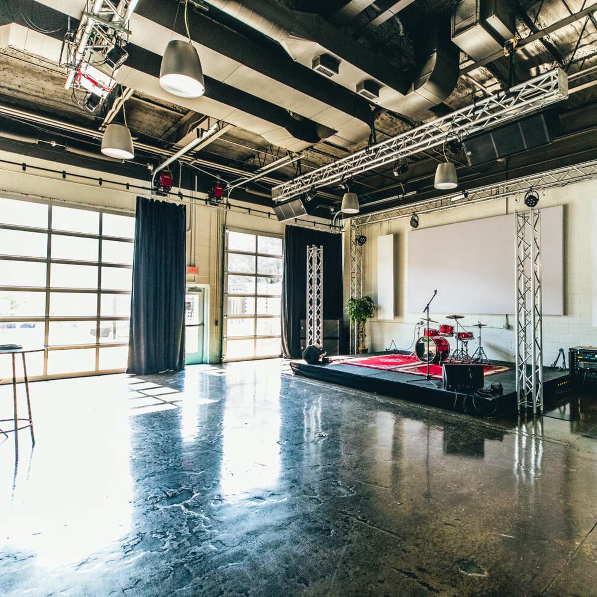 A spacious performance venue featuring a stage with musical instruments, large windows, and industrial-style lighting fixtures.