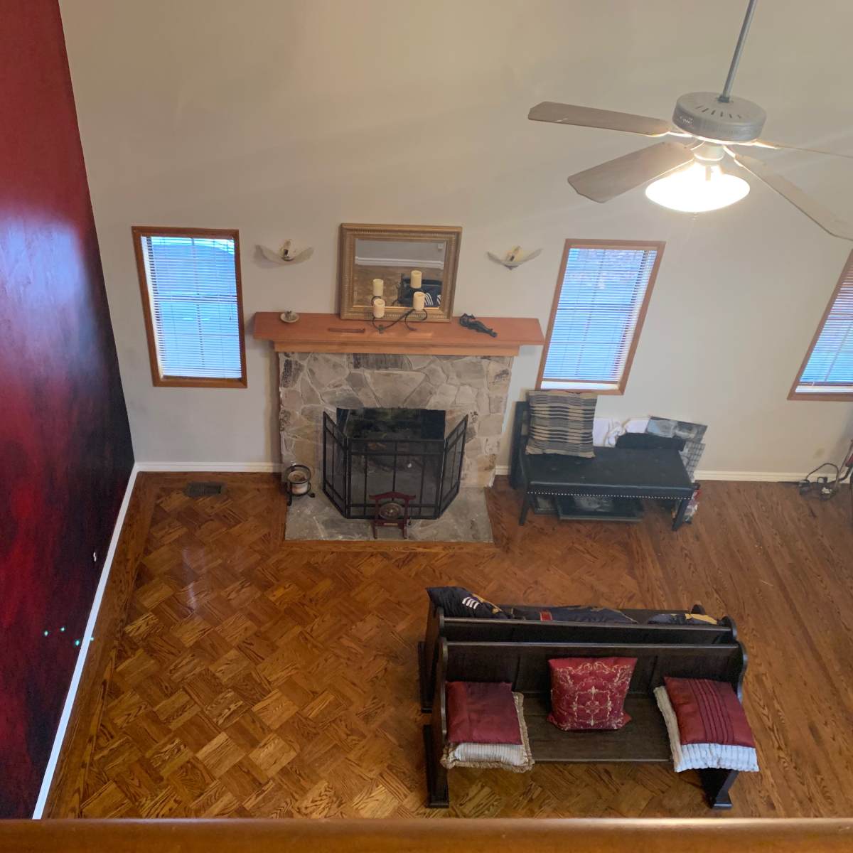 A spacious living room with a stone fireplace, wooden floor, and a red accent wall.