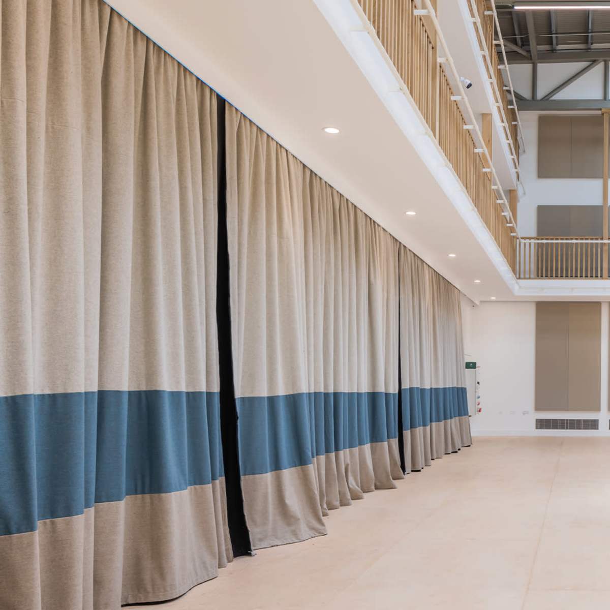 A spacious interior with high ceilings, large windows, and beige curtains featuring blue stripes along one wall.
