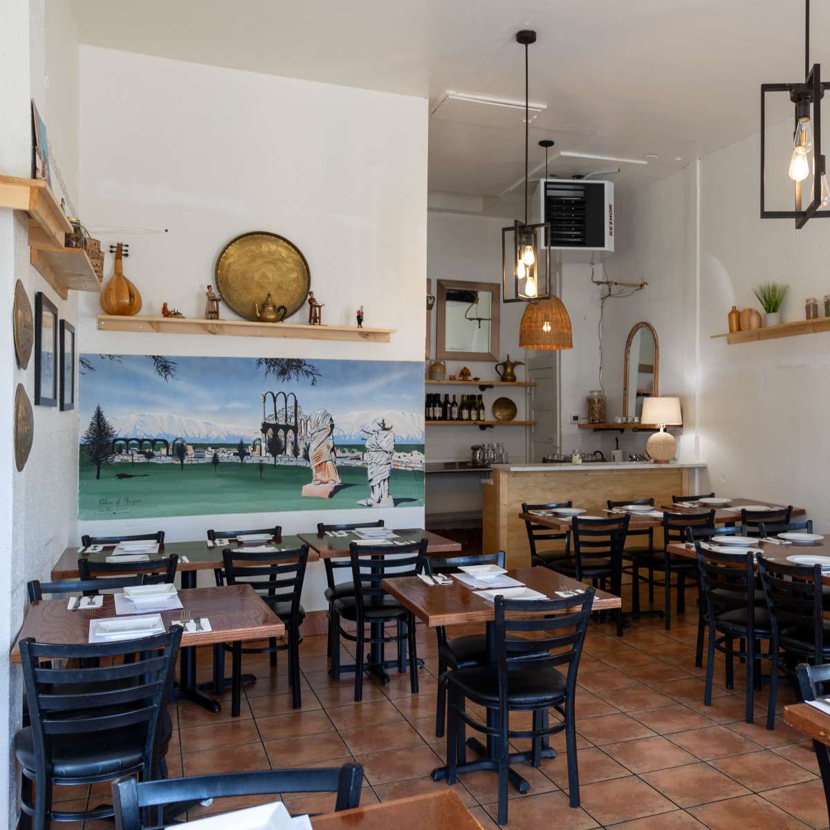A restaurant interior with wooden tables, black chairs, and a mural on the wall depicting a landscape.