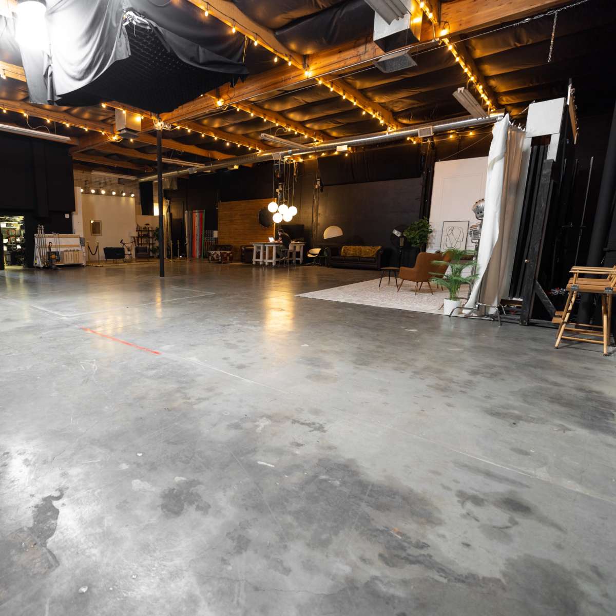 A large, empty studio space with concrete flooring, exposed ceiling beams, and scattered furniture along the back wall.