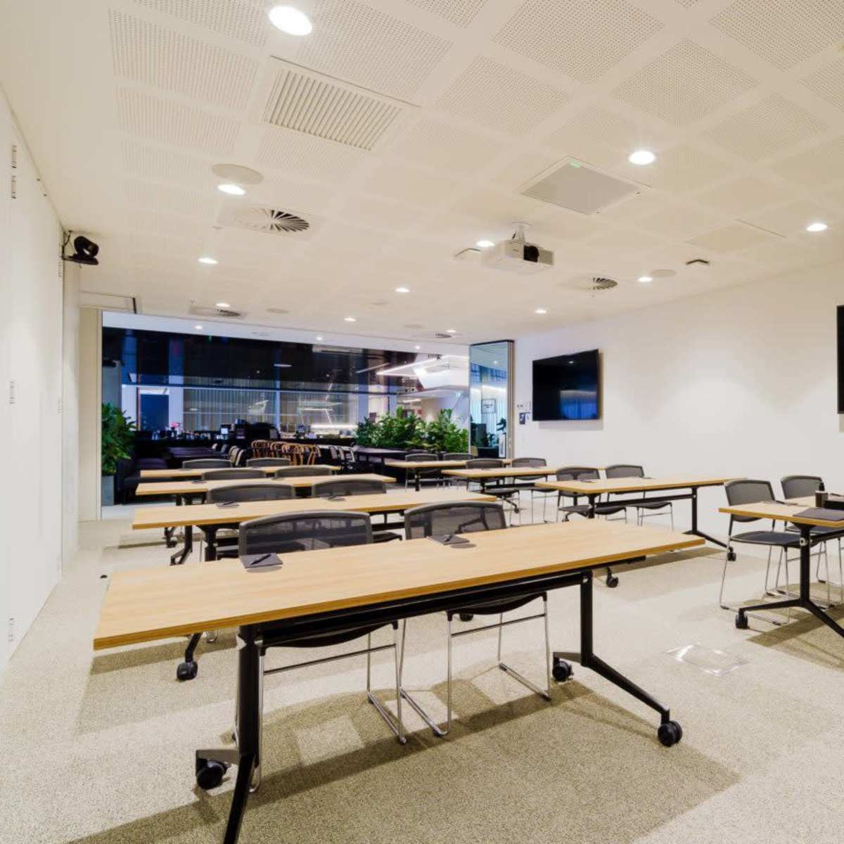 A modern classroom setting with rows of tables and chairs, a podium, and large screens on the walls.