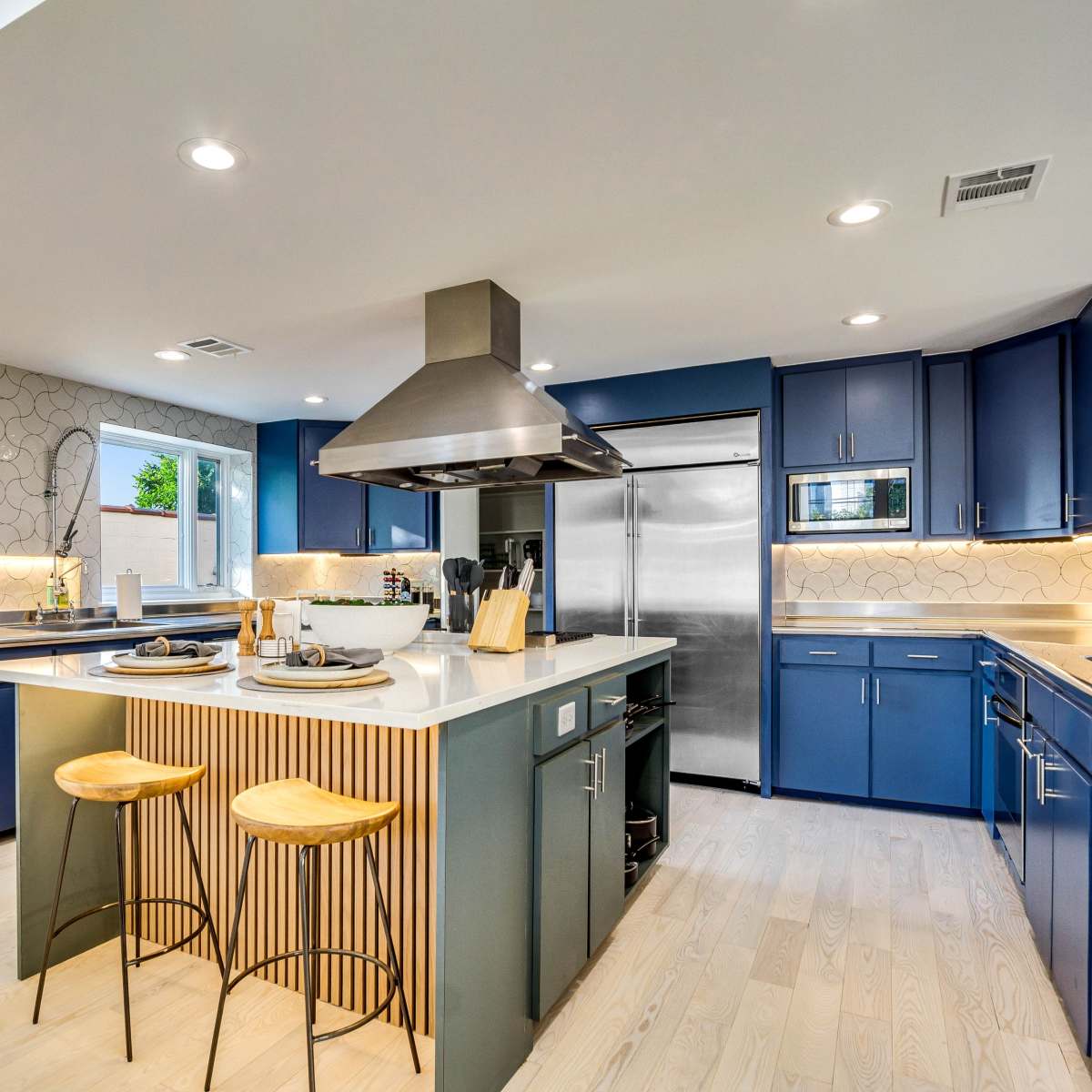 A modern kitchen features blue cabinetry, stainless steel appliances, and a central island with wooden stools.