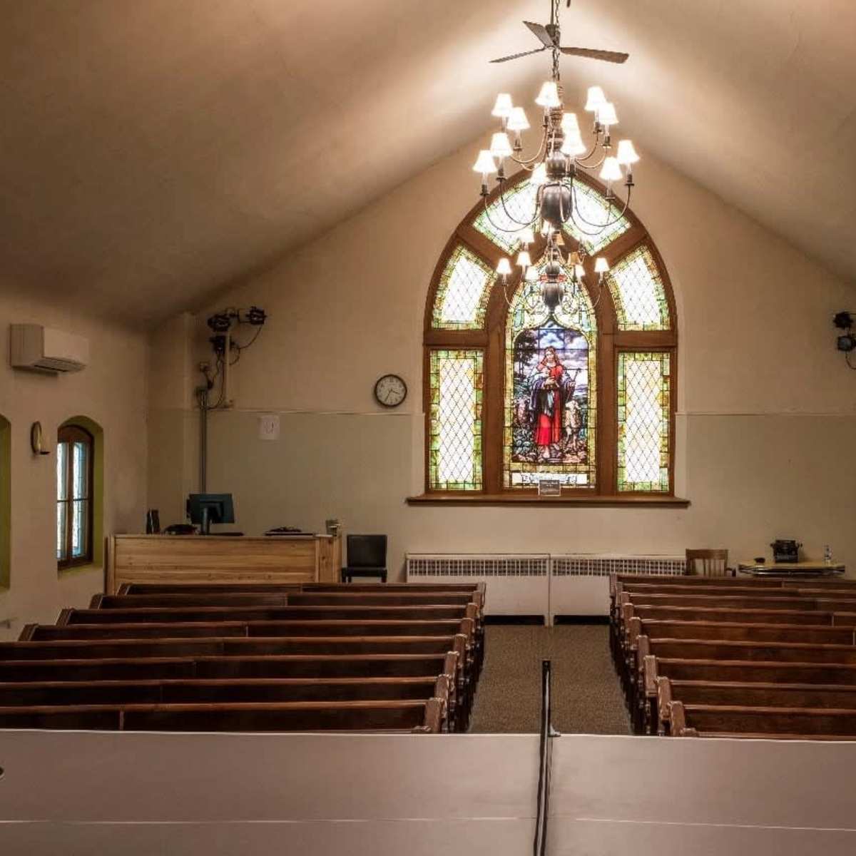 The interior of a church with wooden pews facing a stained glass window at the front.