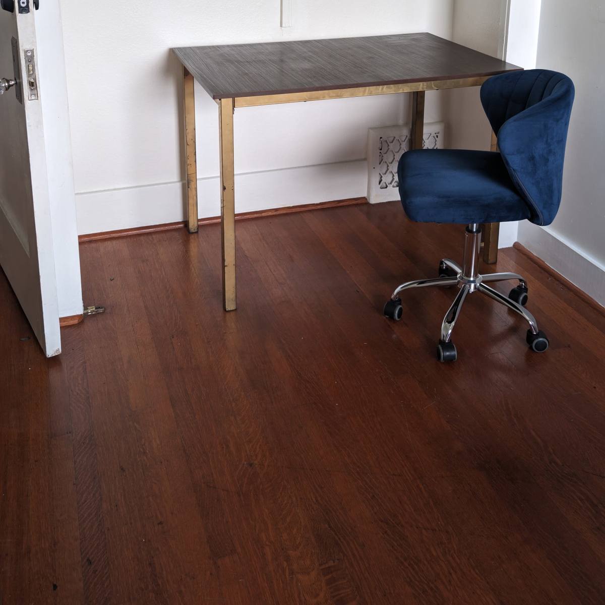 A simple room features a wooden desk and a blue swivel chair positioned next to an open closet.