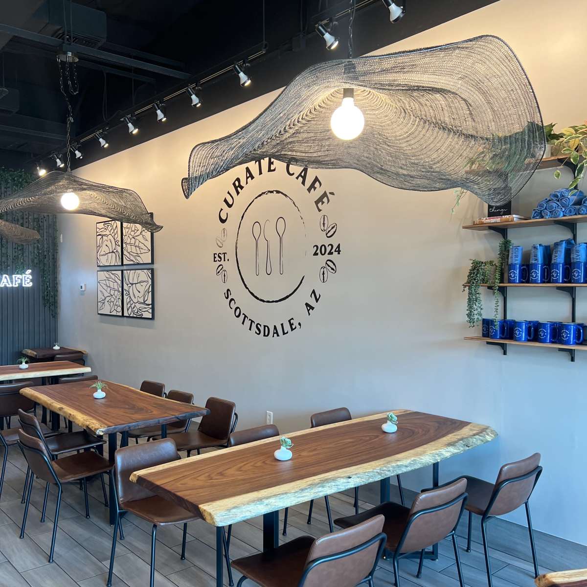 The interior of Curate Café in Scottsdale, AZ, featuring wooden tables and chairs beneath a distinctive wall design with a large café logo.