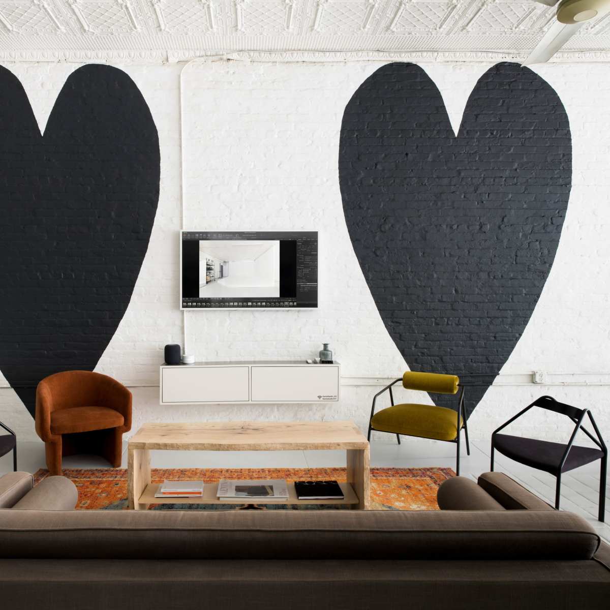 A modern living space with two large black heart shapes painted on the white brick walls and a combination of furniture including a coffee table, a gray sofa, and various chairs.