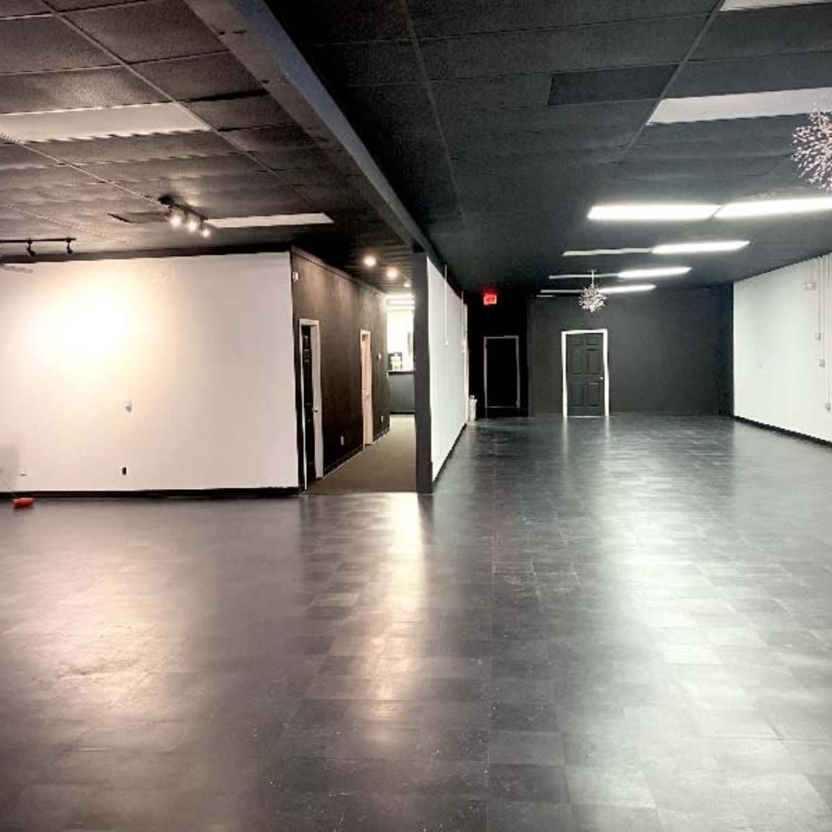 A spacious, empty interior room with black tiled flooring, white and black walls, and large overhead lights.
