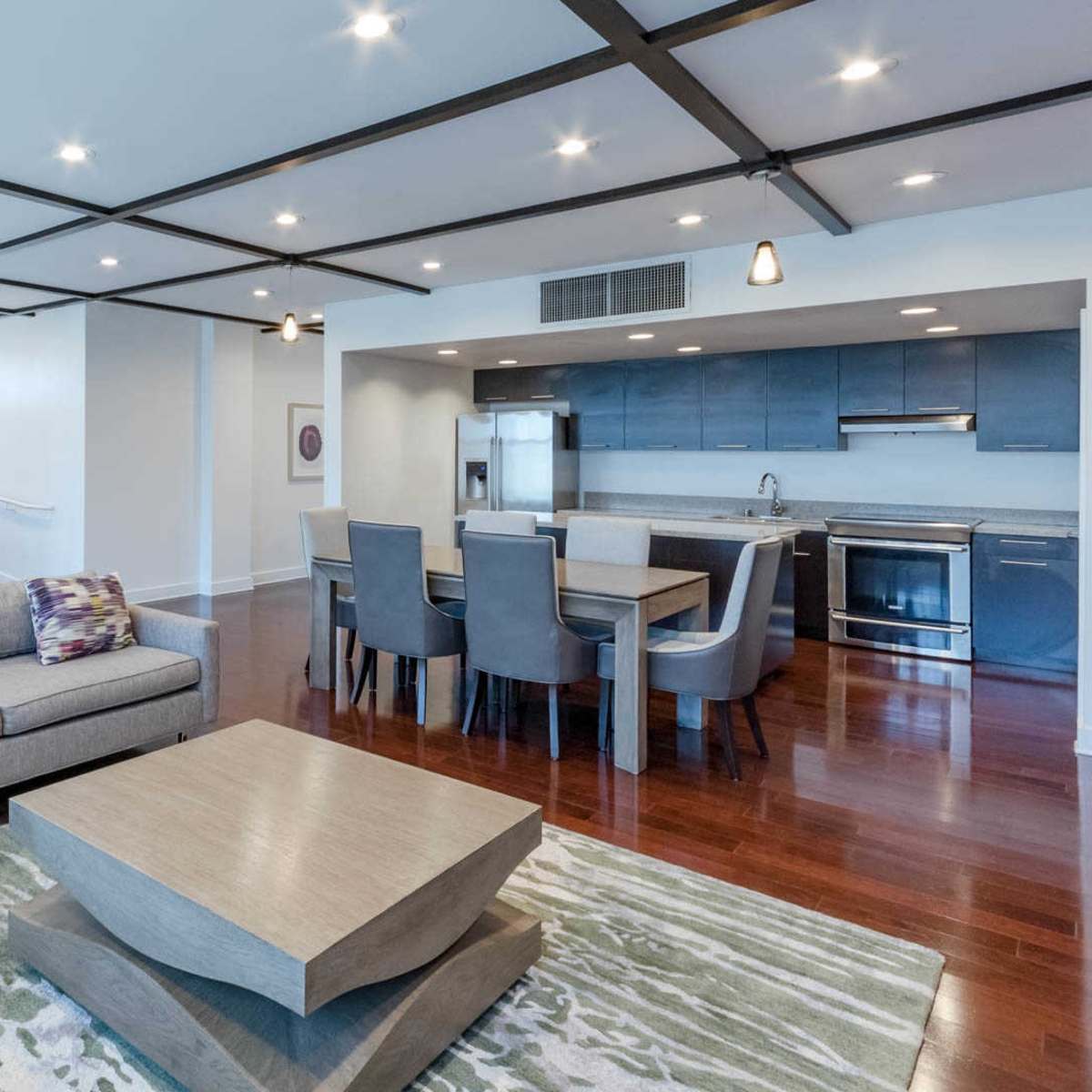 A modern living room with gray sofas, a large coffee table, and a dining area adjacent to a kitchen.