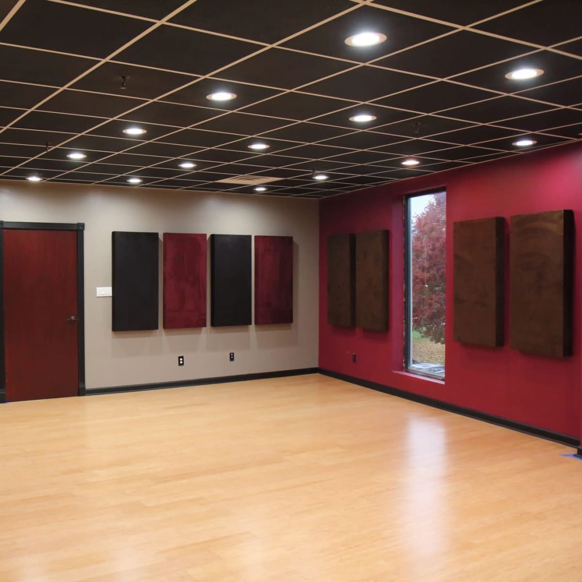 A soundproof room with black and maroon walls, wooden flooring, and several mounted acoustic panels.