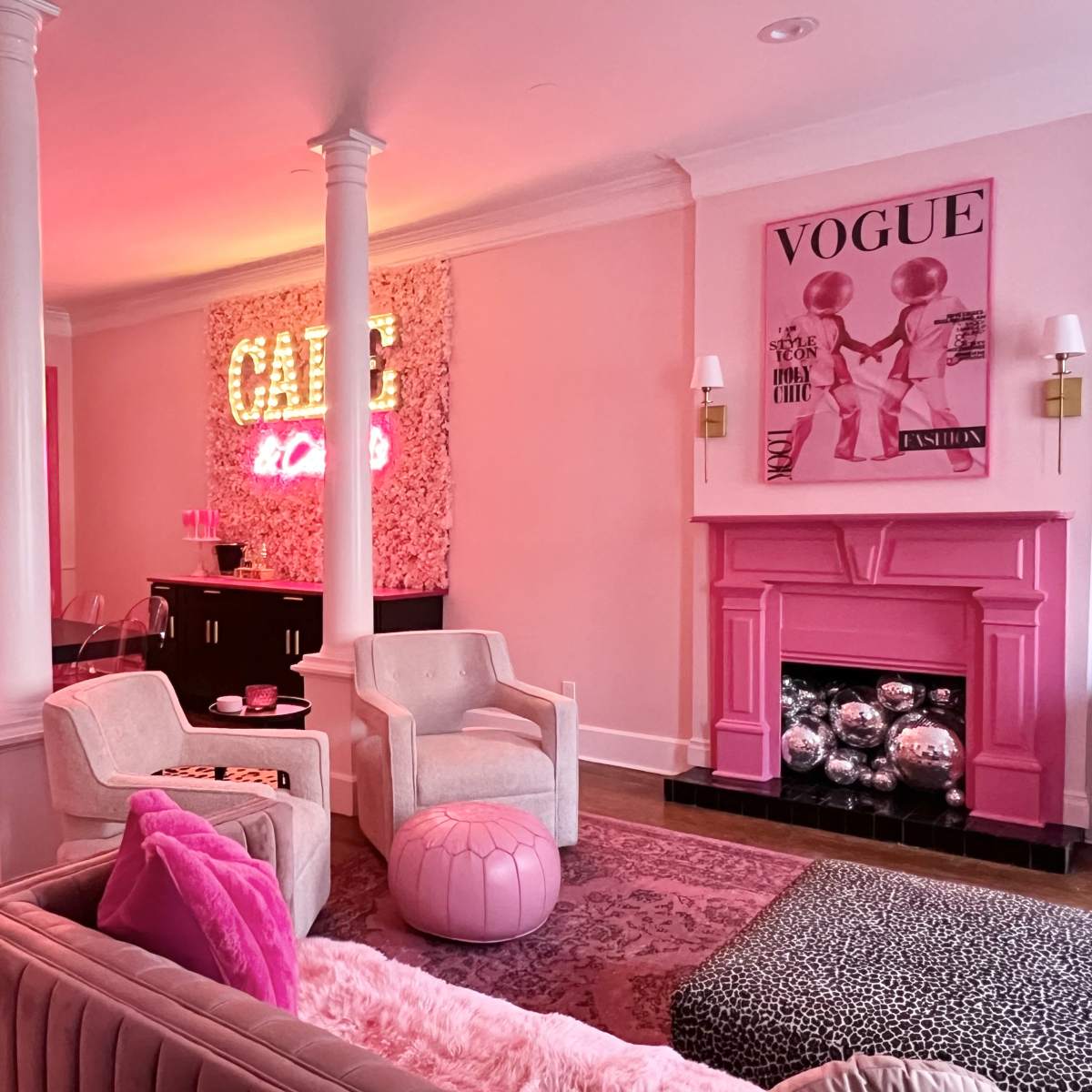 A pink-themed living room with plush furniture, a neon sign, and a dining area featuring a glass table.