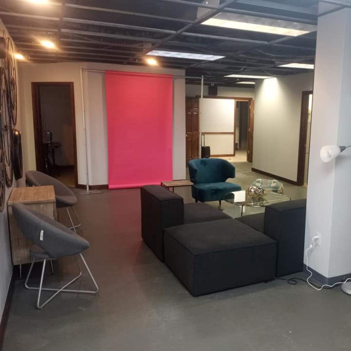 A modern office space featuring a seating area with a dark sofa, light blue chairs, a glass coffee table, and a bright pink backdrop.