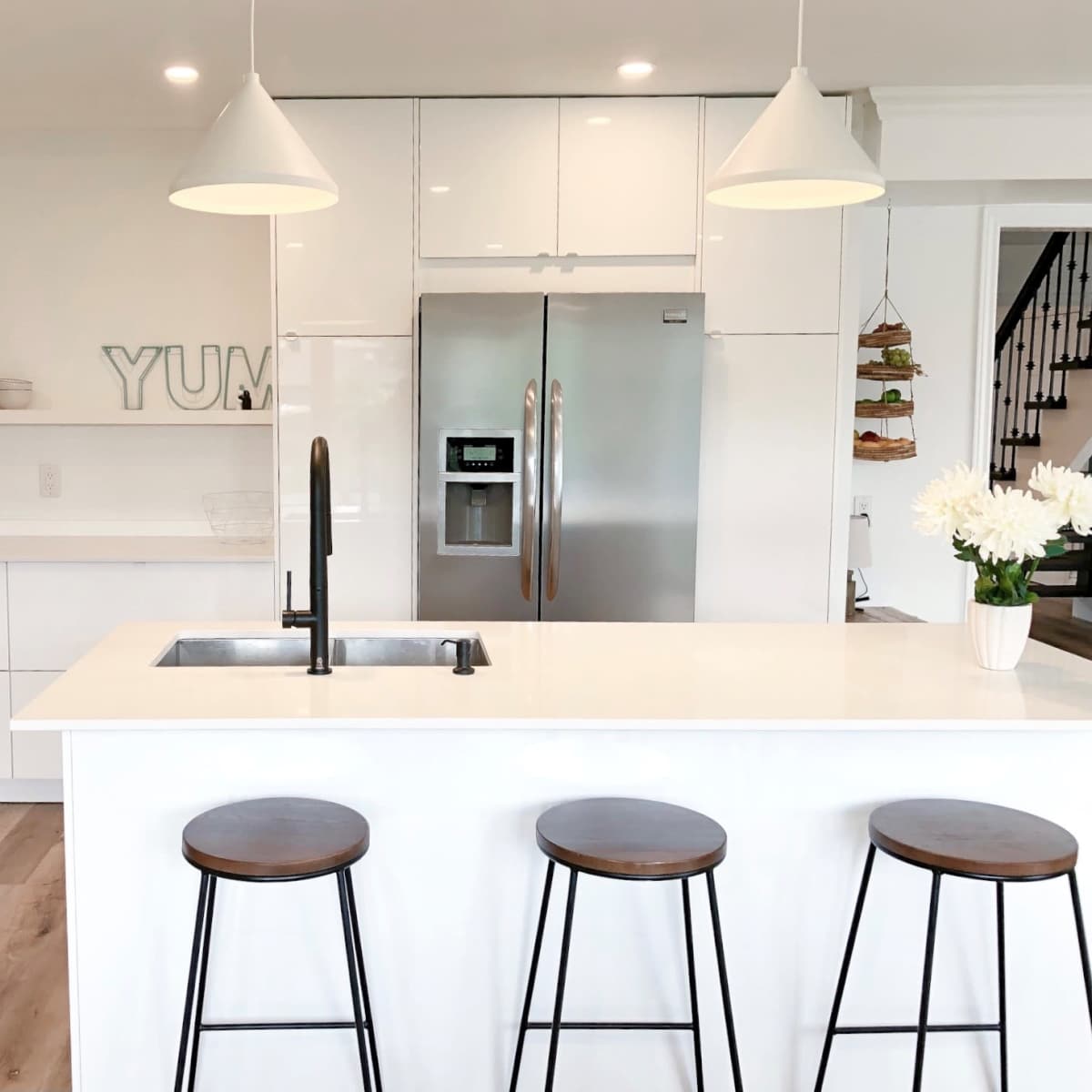 A modern kitchen features white cabinetry, stainless steel appliances, a central island with a sink, and three wooden stools.