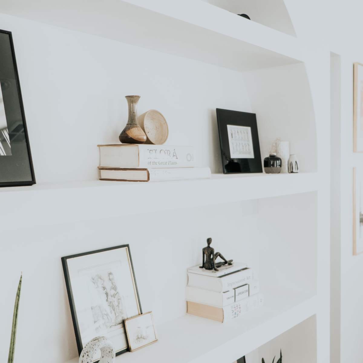 A series of neatly arranged shelves display various framed pictures, decorative objects, and books in a bright environment.