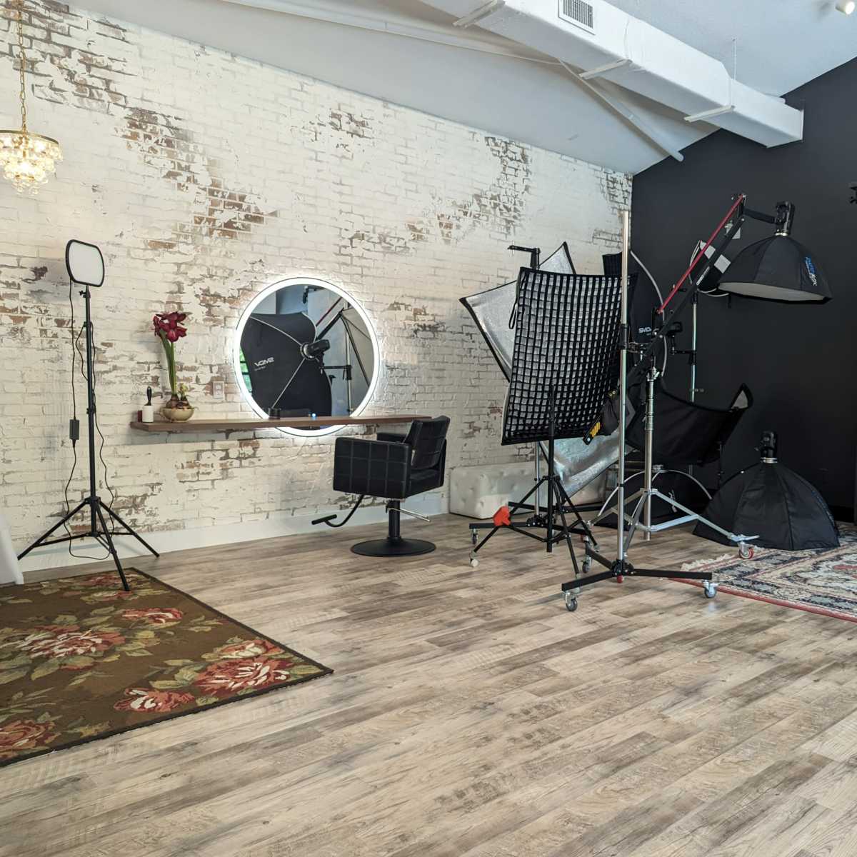 A photography studio with a wooden floor, a backdrop, softboxes, a mirror, and a large floral rug.
