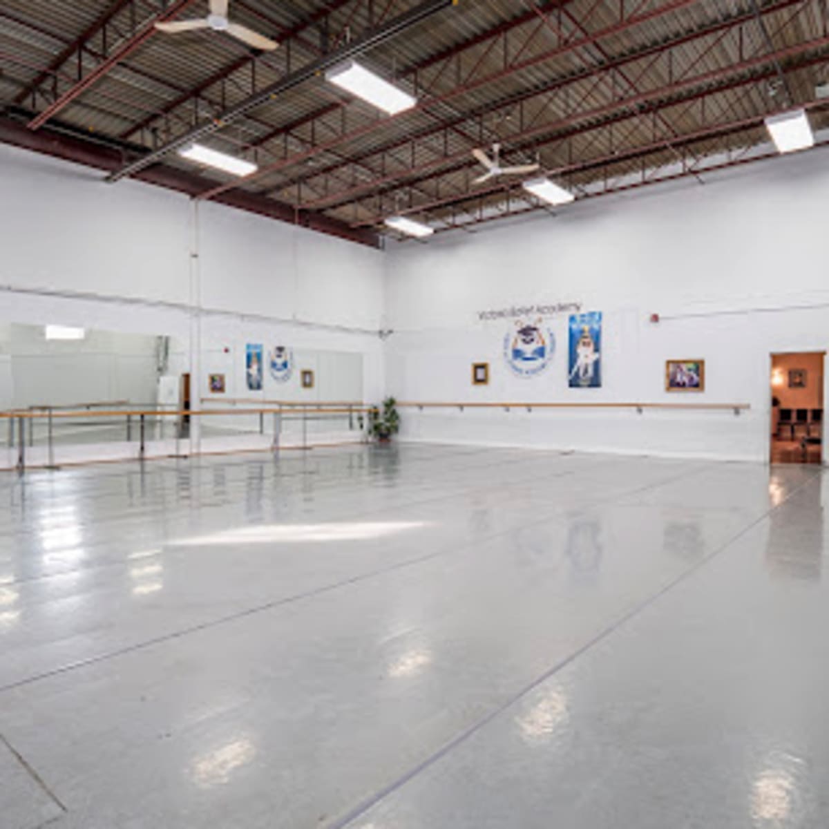A spacious dance studio with mirrors along one wall, polished concrete floors, and a few framed artworks.