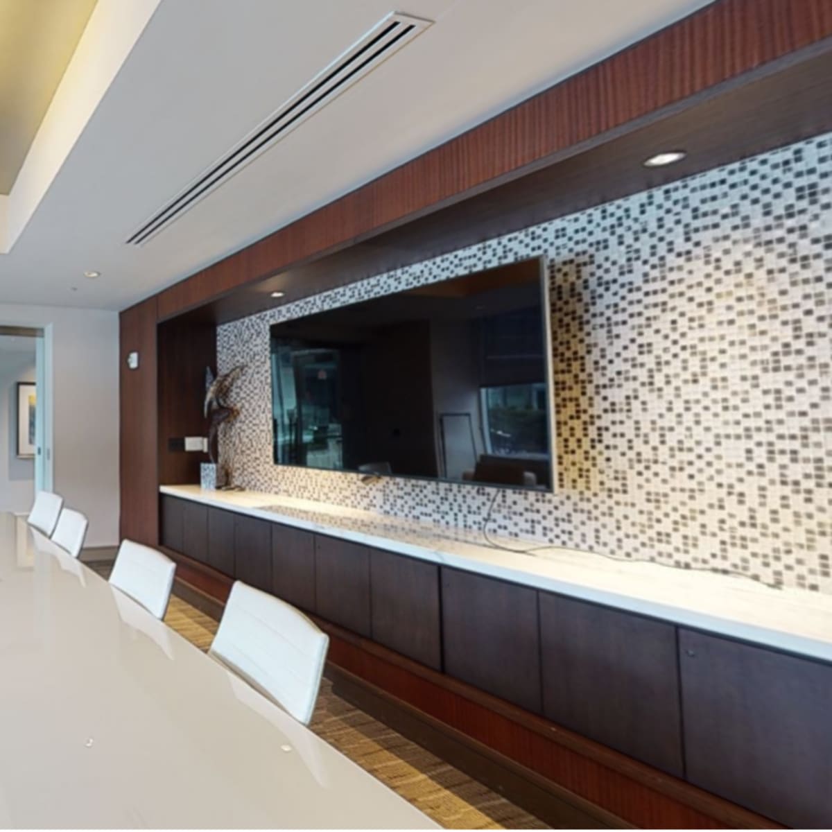 A modern conference room with a long white table, white chairs, and a wall-mounted television along with decorative tile accents.