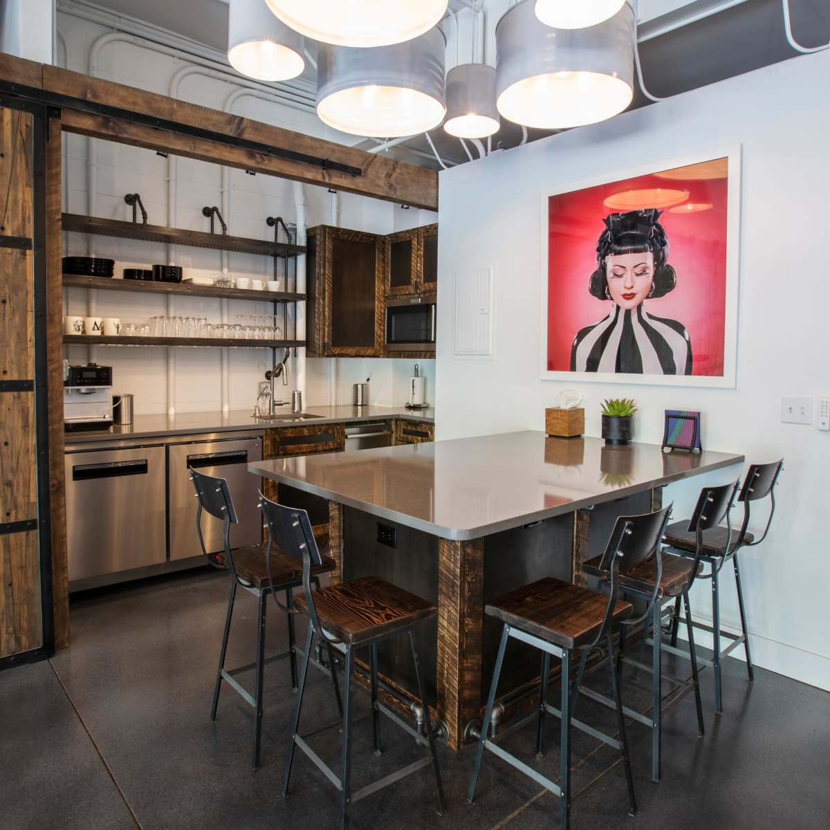 A modern kitchen with a large island, bar stools, stainless steel appliances, and a framed artwork on the wall.