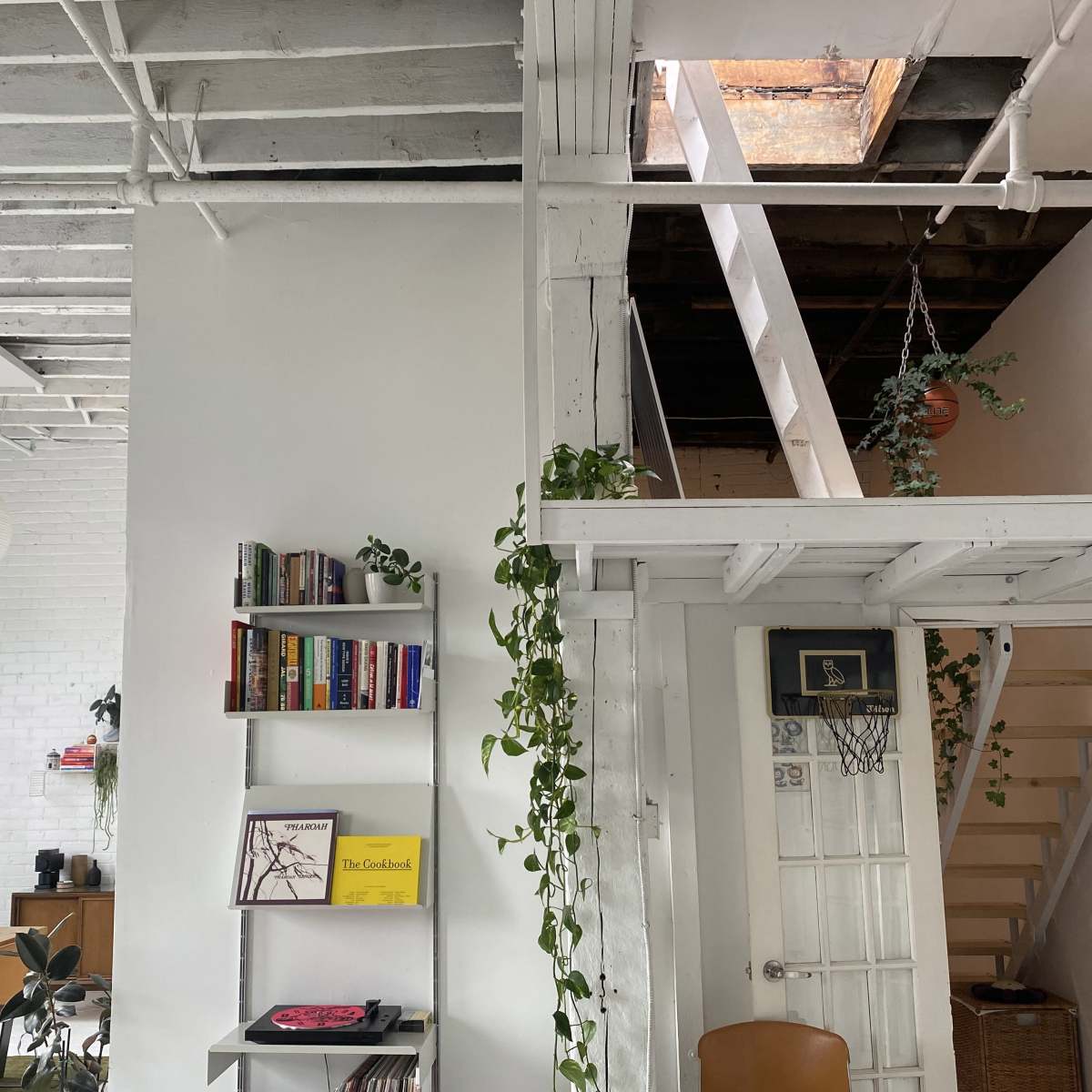 An interior space featuring a staircase, a bookshelf, plants hanging from the ceiling, and a small skylight.