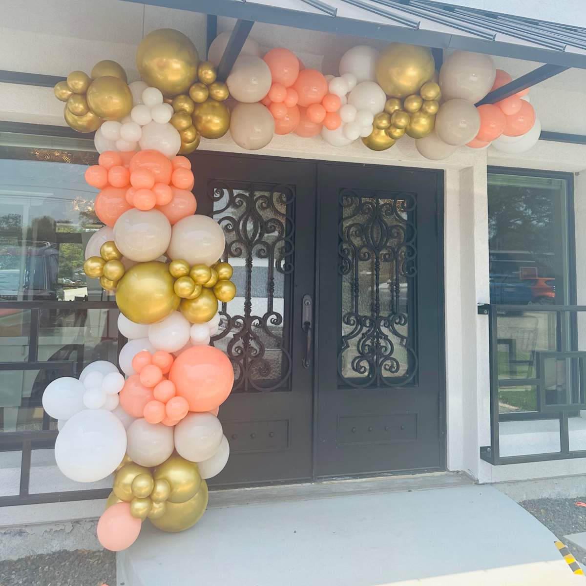 The entrance features a decorative arch made of various balloons in shades of peach, white, and gold.