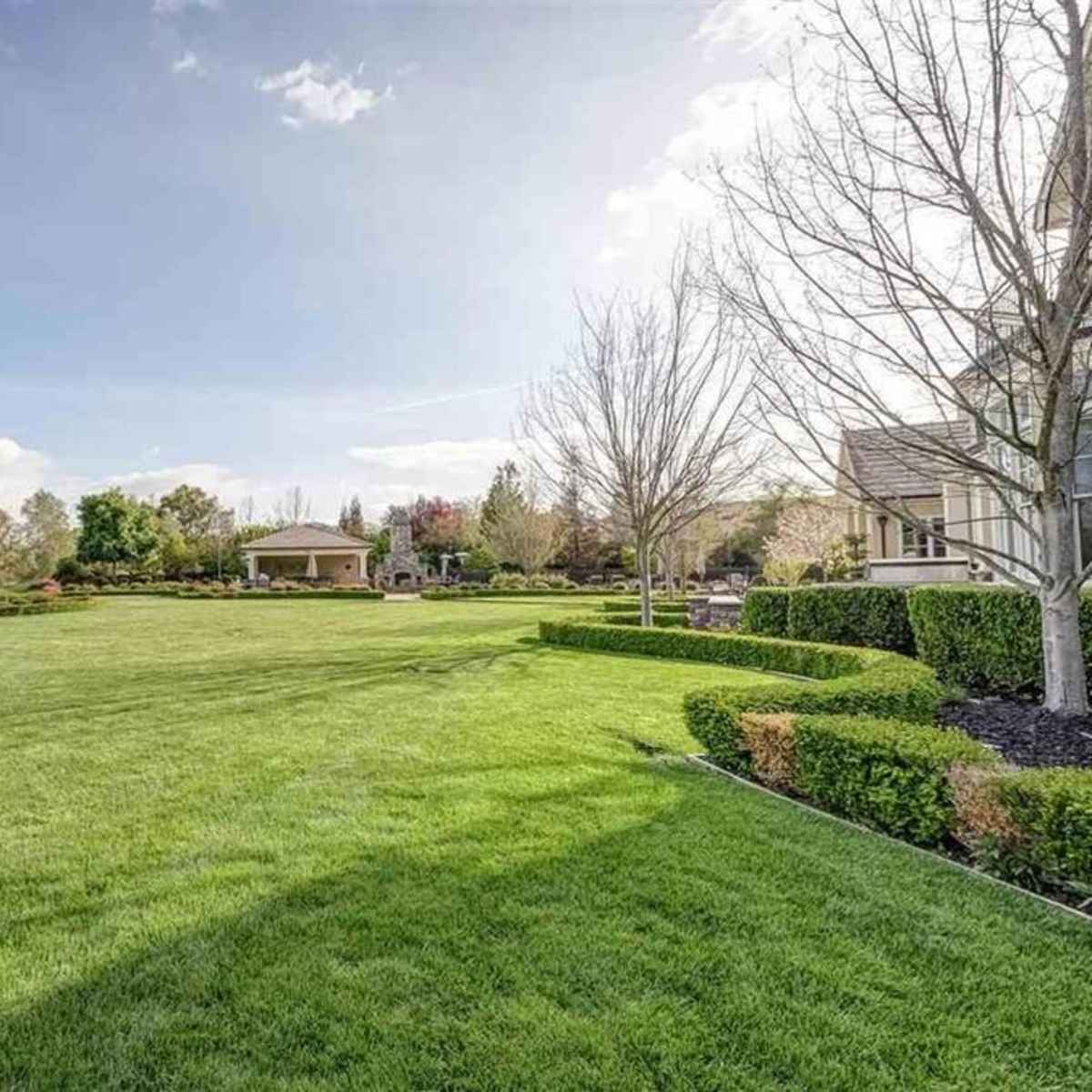A spacious, well-maintained lawn surrounded by trees and a gazebo in a residential area.