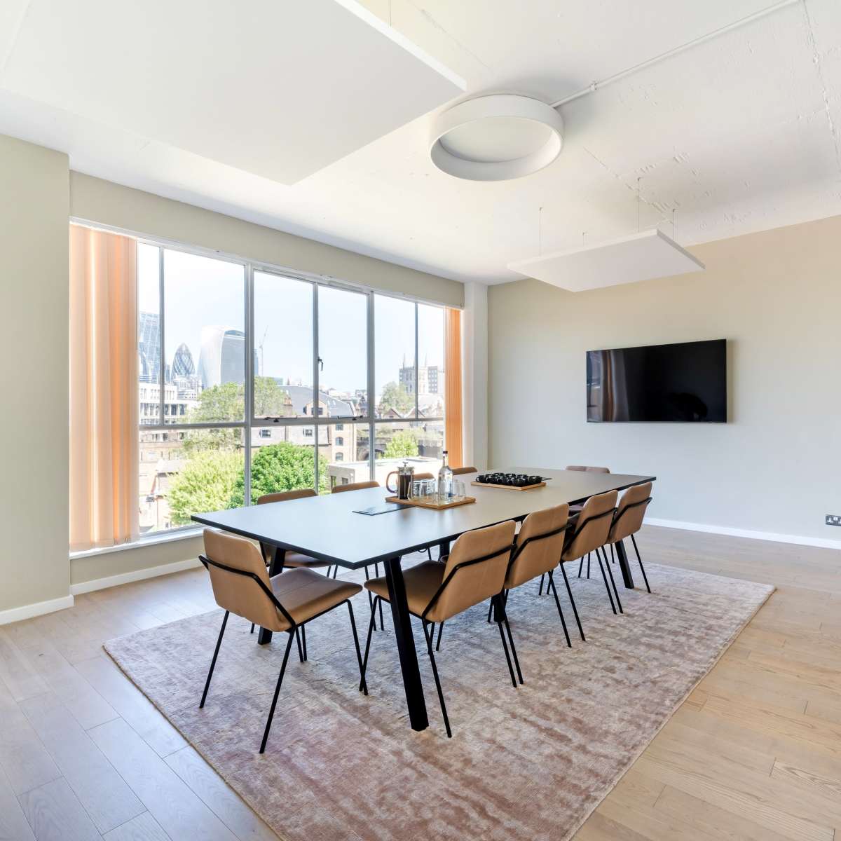 A modern conference room features a long table with eight chairs, large windows with city views, and a wall-mounted television.