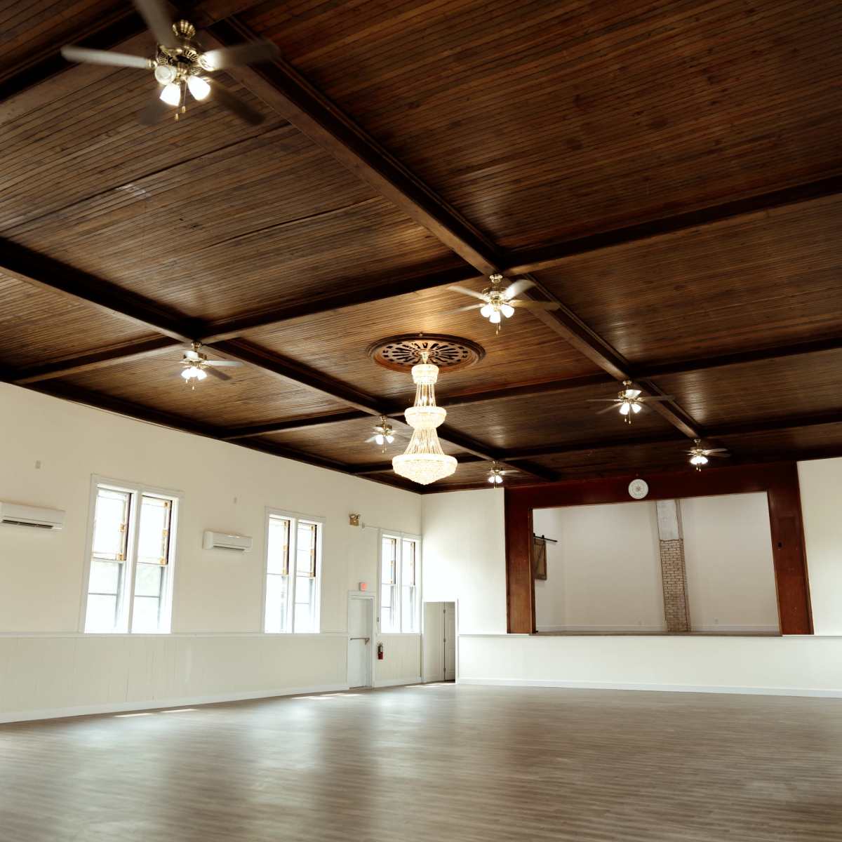 A spacious interior of a hall with wooden walls, a high ceiling with ceiling fans, and a central chandelier.