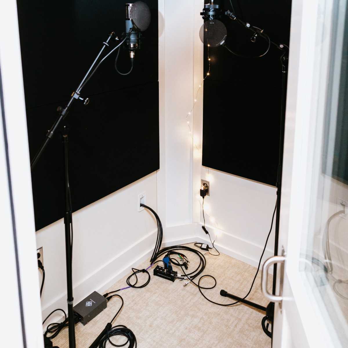 A recording booth with two microphones on adjustable stands and soundproofing panels lining the walls.