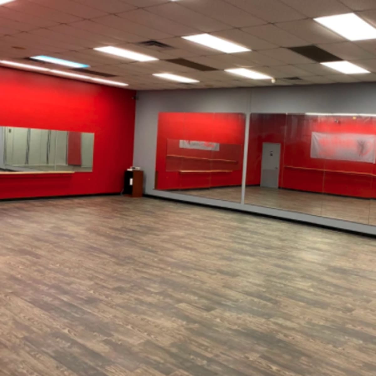 A spacious dance studio with red walls, a mirrored wall, and wooden flooring.