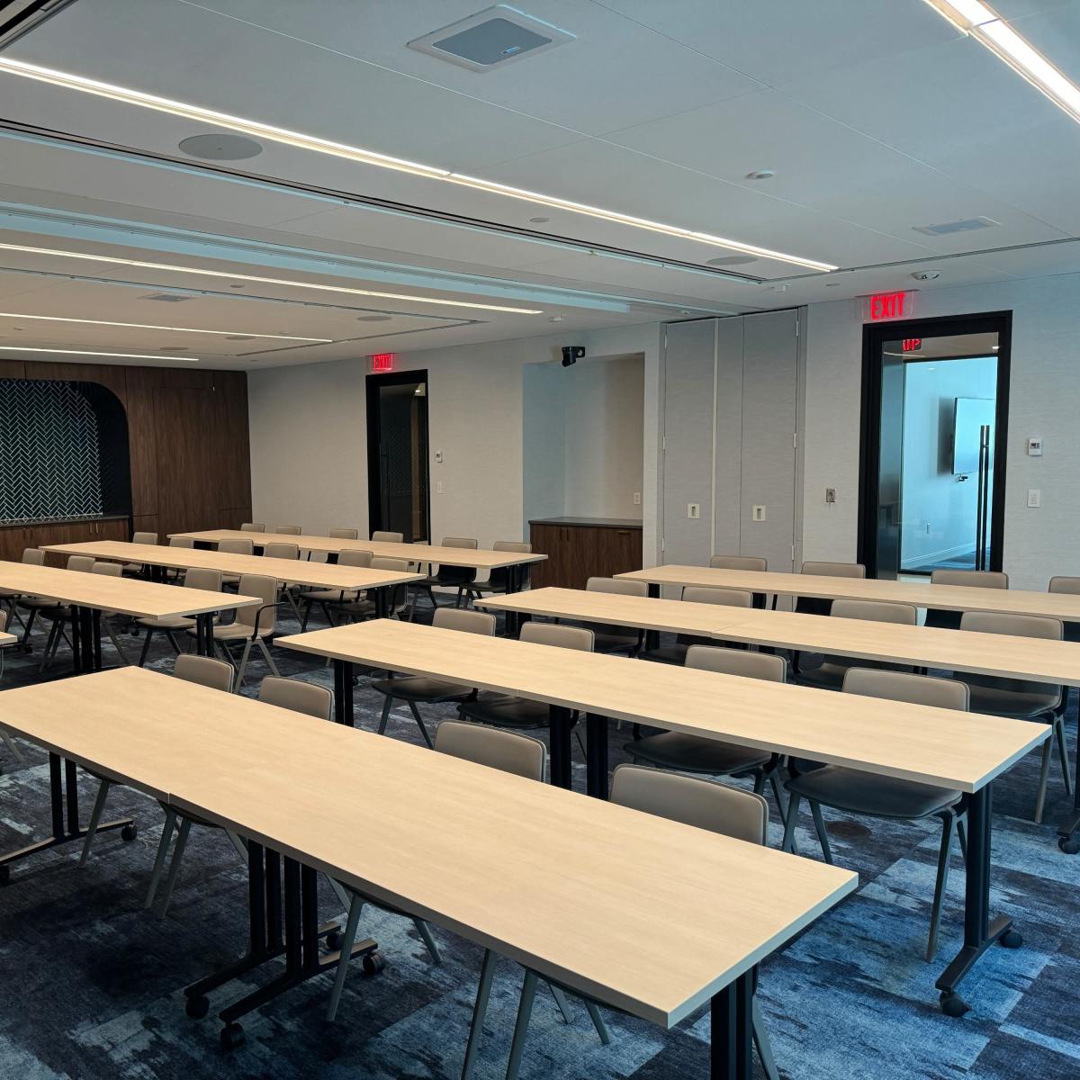 A classroom is arranged with multiple rows of tables and chairs, ready for an event or meeting, with modern decor and lighting.