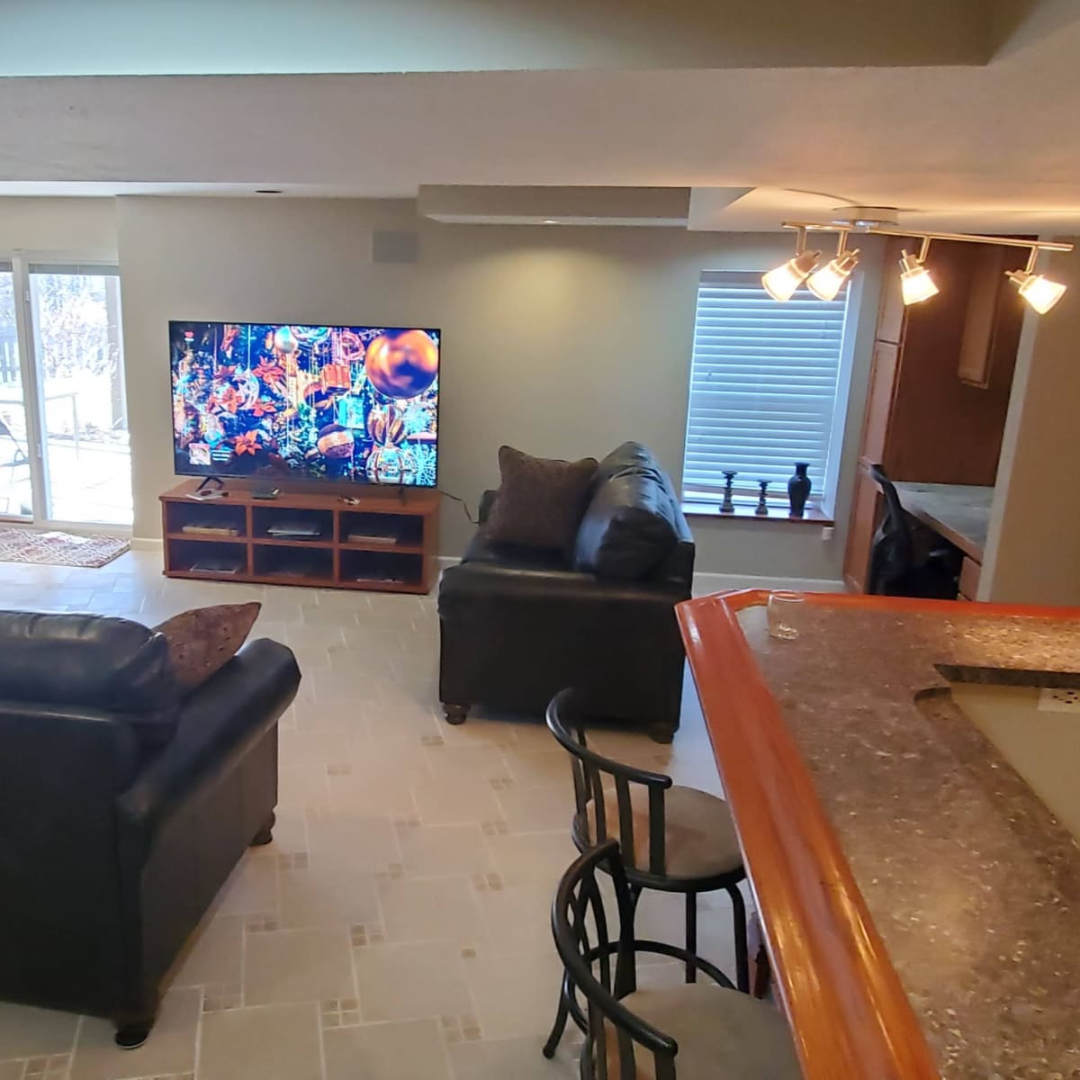 A spacious living area features a television, seating, and a bar counter, with large windows allowing natural light.