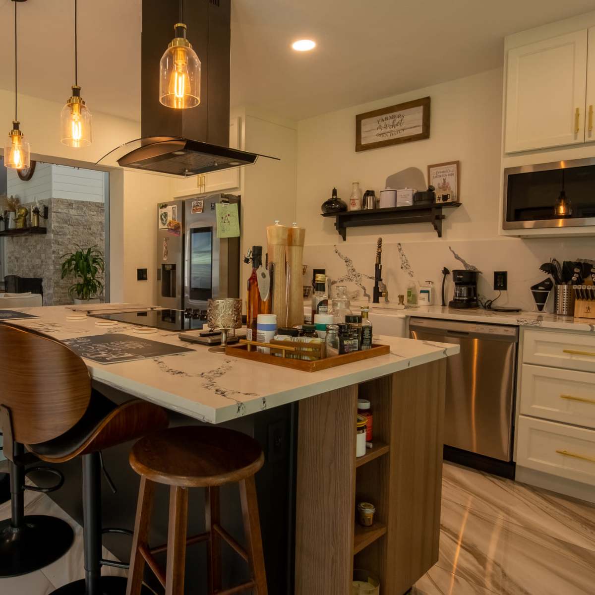 A modern kitchen with a central island, bar stools, and various cooking appliances arranged along the countertops.