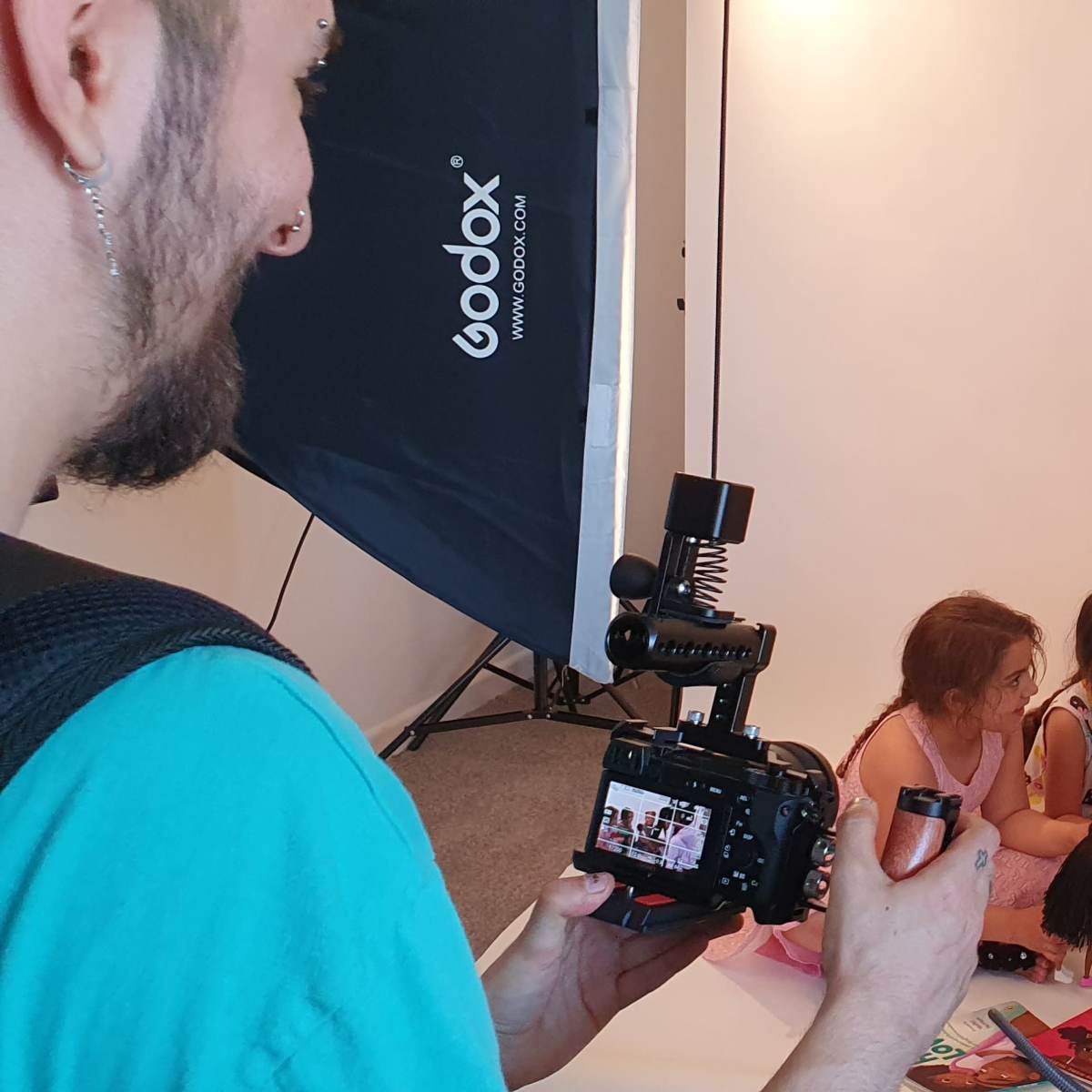 A man and three young girls are sitting on the floor in a photography studio, surrounded by cameras and lighting equipment.