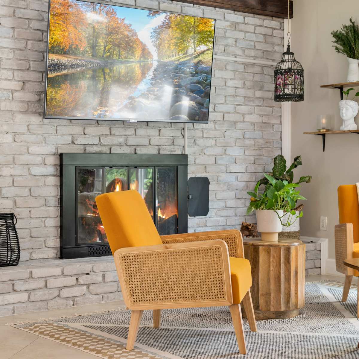 A modern living room features two yellow chairs facing a round wooden table, with a stone fireplace and a television mounted above it.