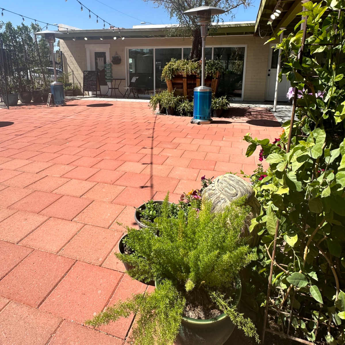 A landscaped courtyard features a brick patio, potted plants, and a sunlit building in the background.
