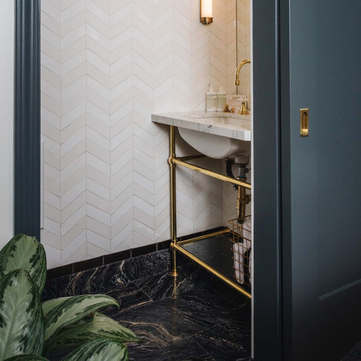 A modern bathroom features a herringbone patterned wall, gold accents, and a marble countertop with a sink.