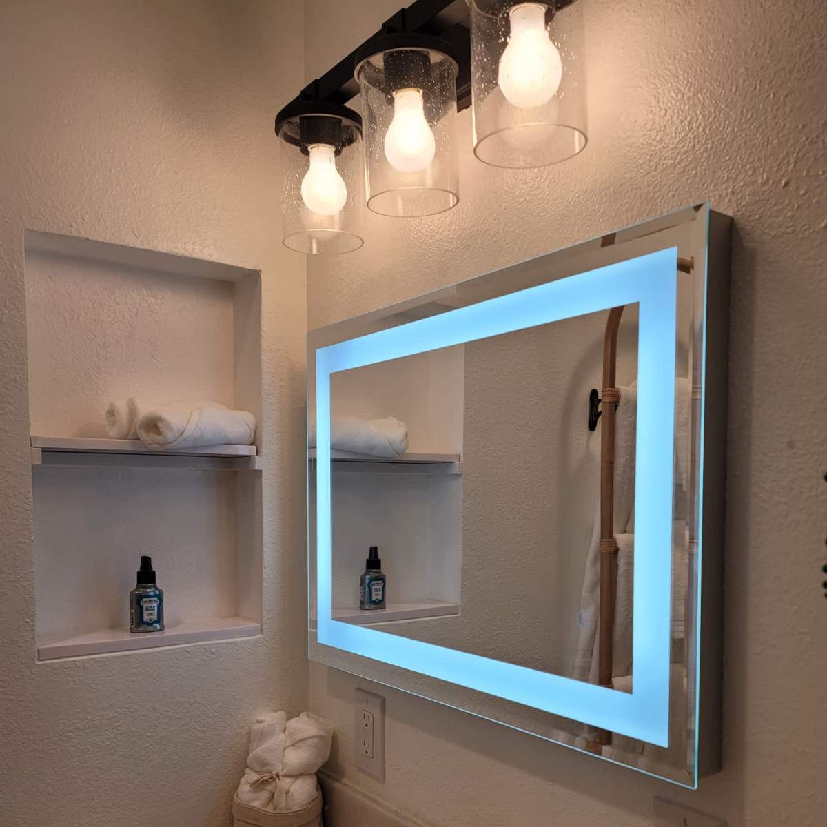 A modern bathroom with a backlit mirror, a marble countertop sink, and a light fixture above the mirror.