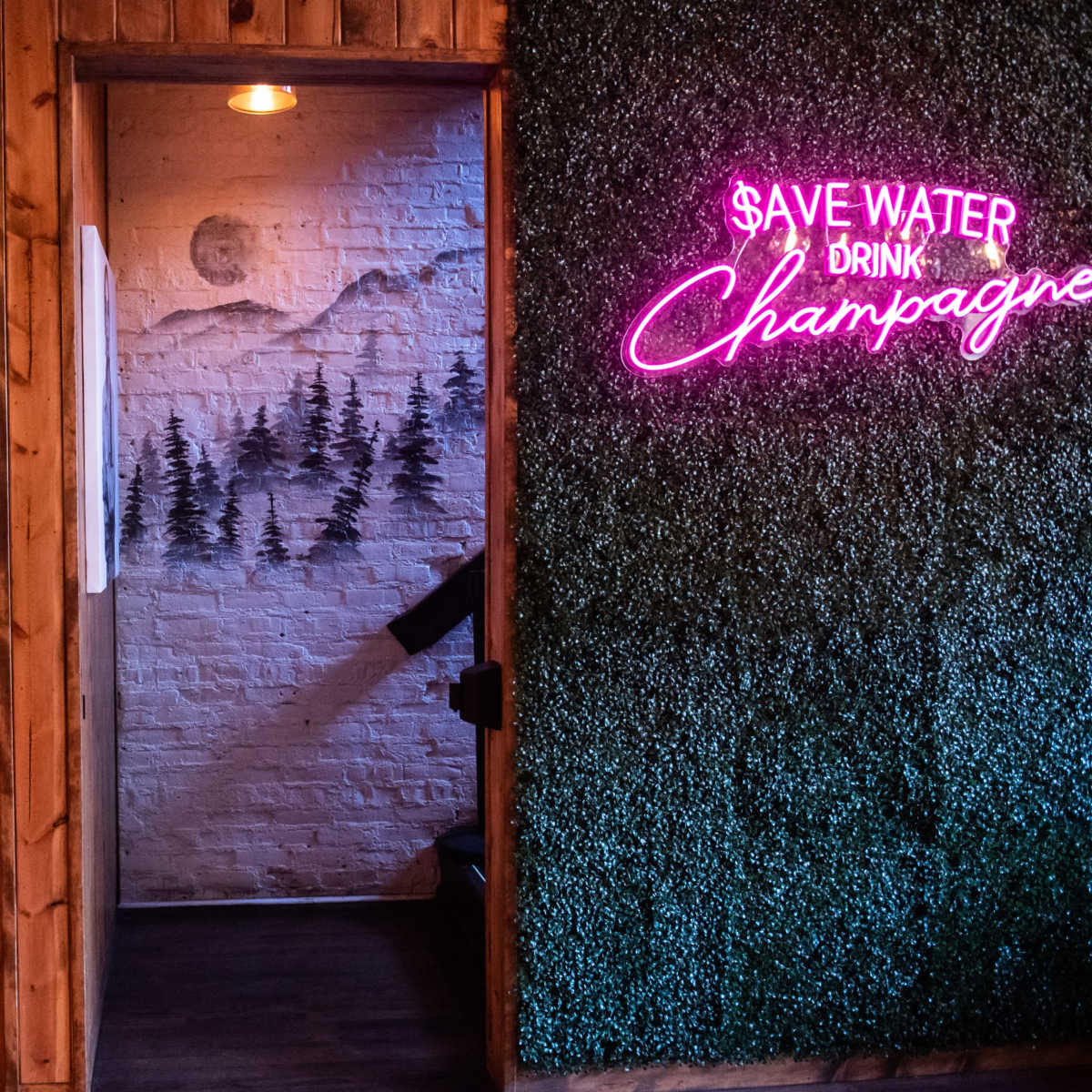 A restaurant interior featuring a cozy booth, a mirror, and a neon sign on a grass-covered wall.